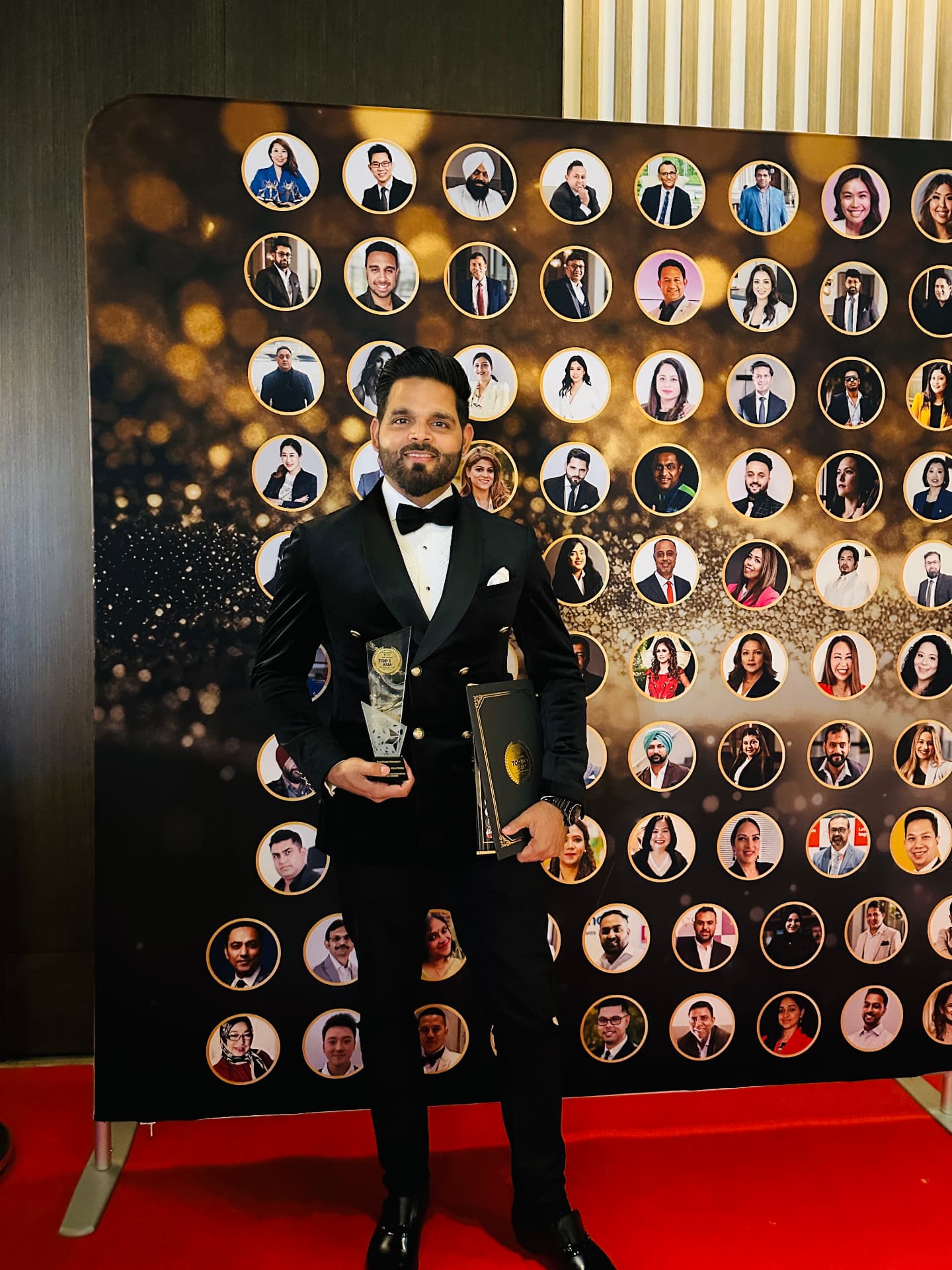 Irshad Siddiqui with his Top 100 trophy in front of the winners wall